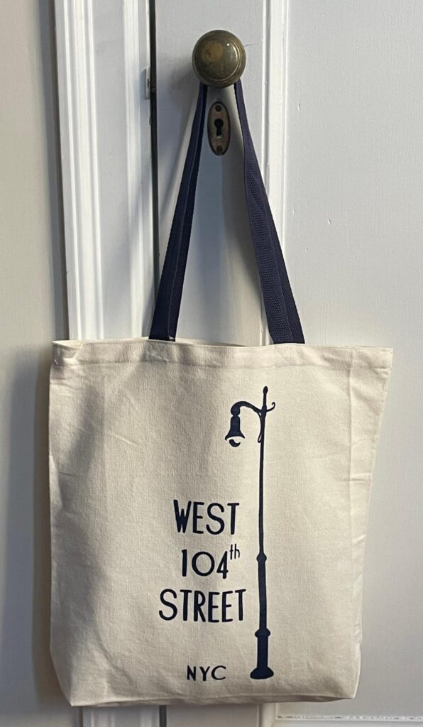 Natural cotton canvas tote bag with navy blue handle and West 104th Street Block Association lamp post logo.