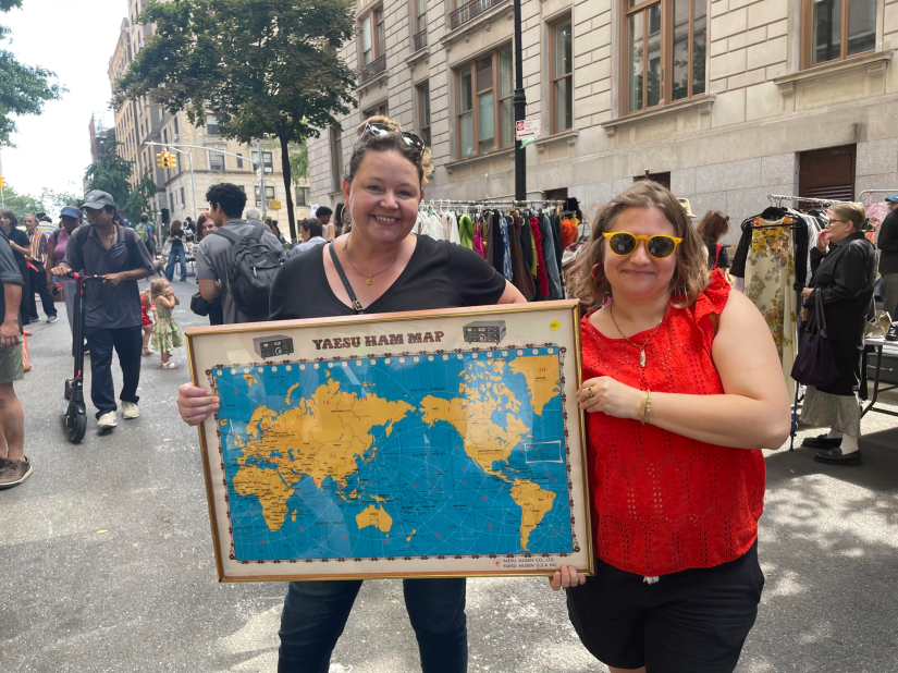 Two smiling women holding a framed world map of ham radio stations.
