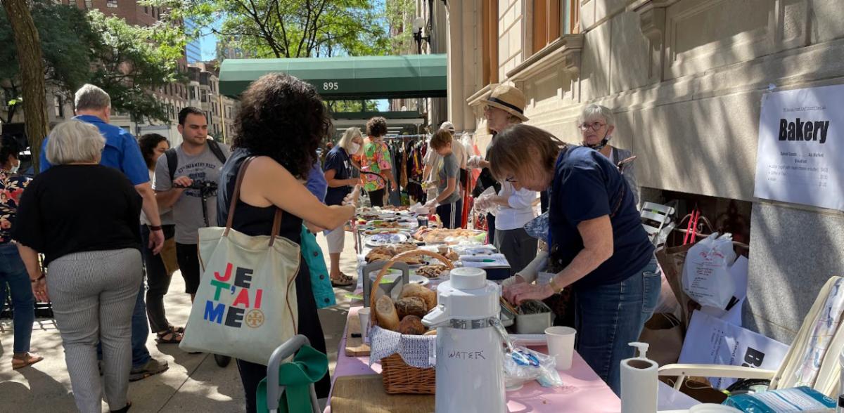 A woman with colorful “Je t’aime” tote bag browsing bakeries at the yard sale.
