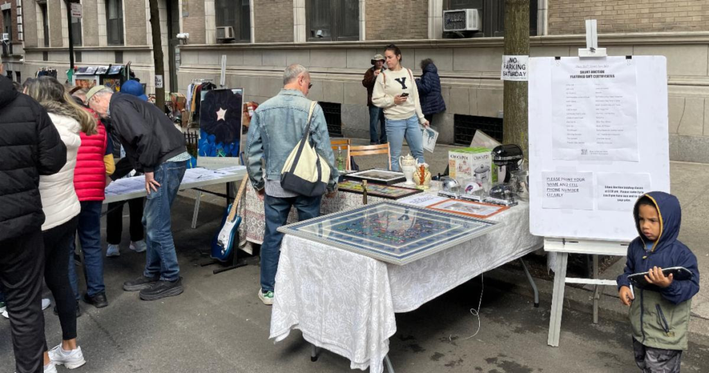Table draped in white tablecloth showcasing items at the silent auction with people browsing items.