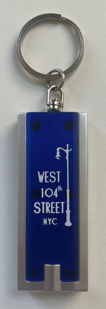 West 104th Street Block Association logo keychain. Blue with white print on, long, rectangular, clear plastic with silver tone trim, ring and LED flashlight.