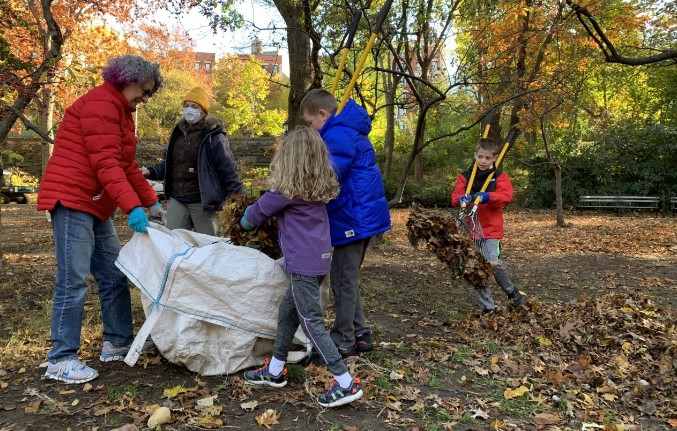 A family raking leaves and putting them in a large whiten trash bag.