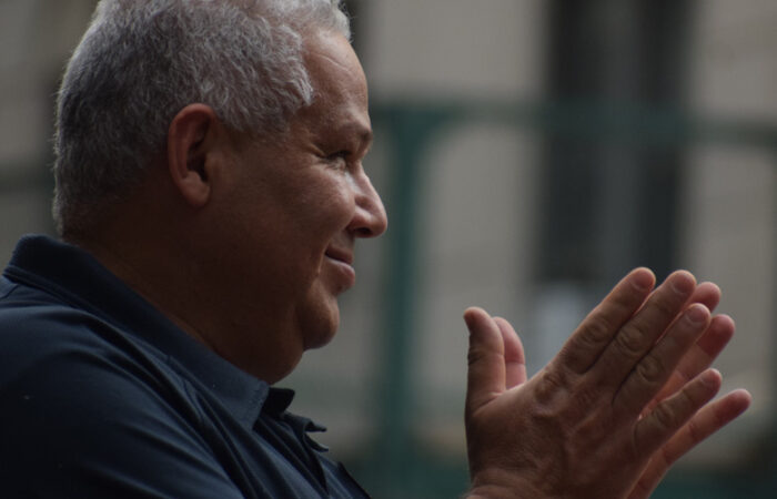 Side view of a whtie haired man smiling and clapping.