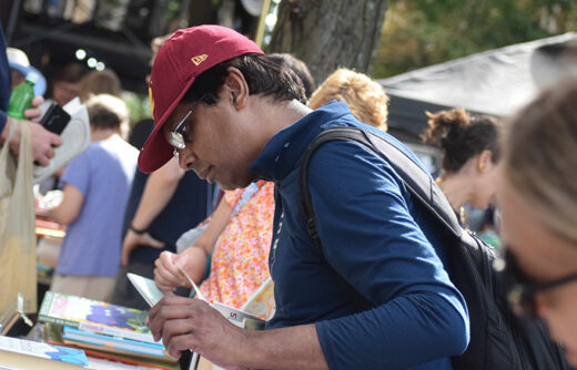 A man in a red baseball cap and glasses examines a book at the book tables
