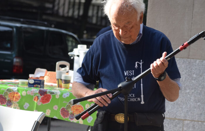 An elderly man with white hair and a navy t-shirt examines a tripod