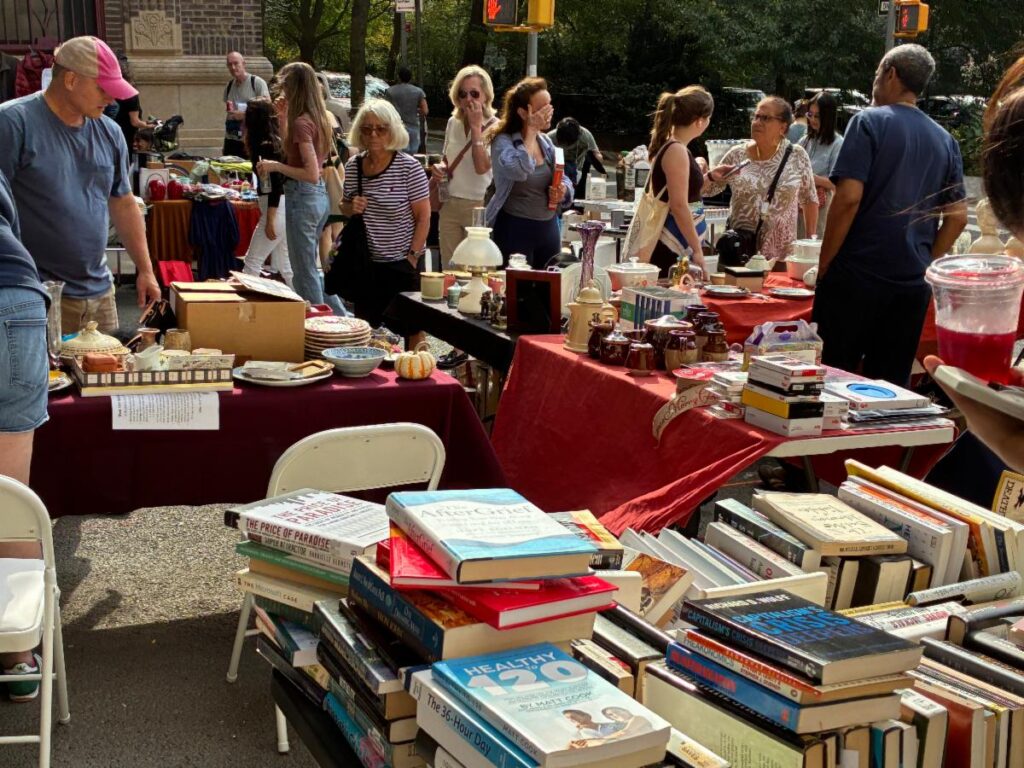 Yard sale street scene. People gathering around tables of books and household goods for sale along West 104th Street.