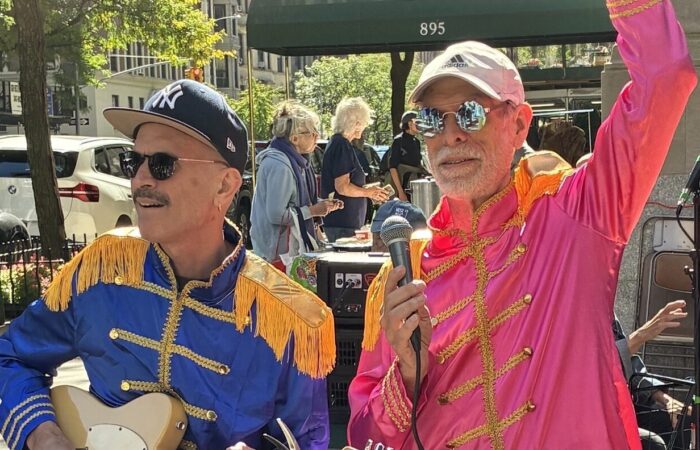 Too middle aged, male band members wear a baseball cap and sunglasses and Sergeant Pepper style satin shirts with gold epaulettes and a microphone